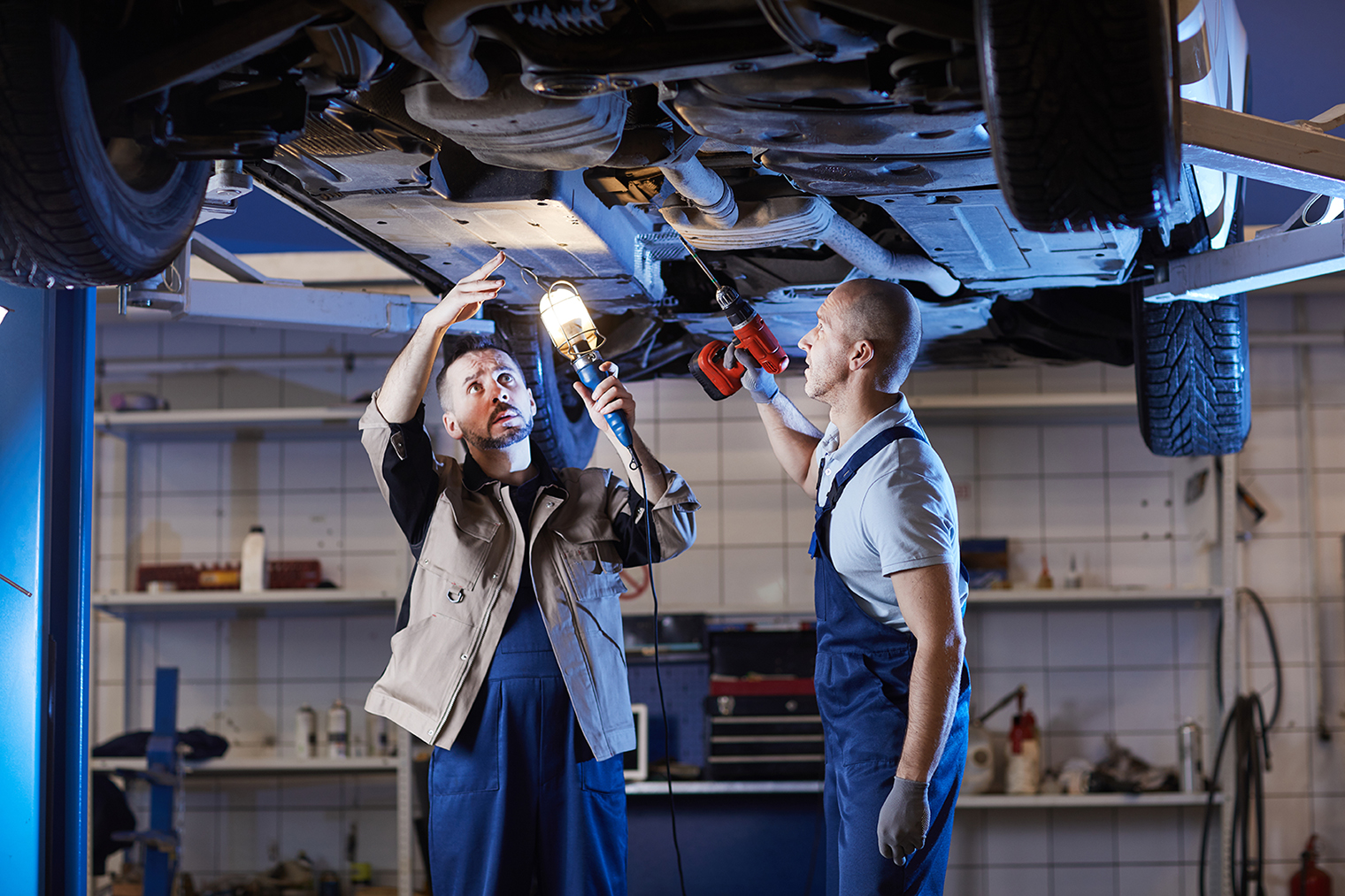 Portrait of two mature mechanics standing under car on lift while inspecting vehicle in auto repair workshop, copy space